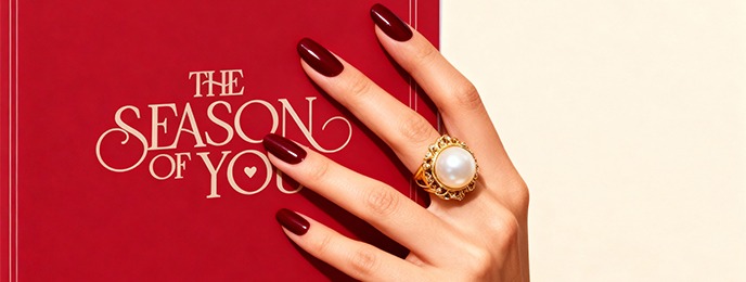 Hand mit roten Nägeln und goldem Perlenring auf rotem Buch