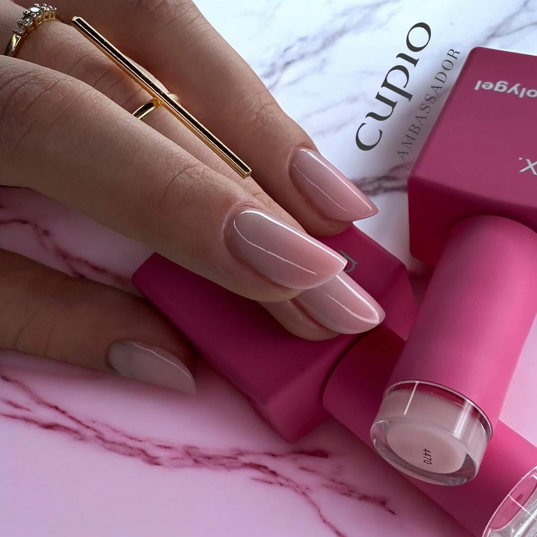 Snapinst-app_480604322_1183665233768839_6131329758475949766_n_1080 Händedetail mit perfekt manikürten Nägeln in Rosa, pinken Nagellackfläschchen und goldenen Ringen auf marmoriertem Untergrund