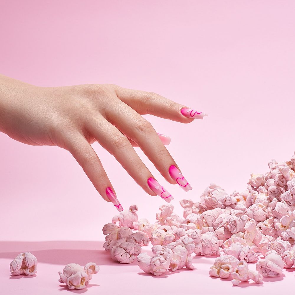 Feminine Hand mit bunten Nägeln in Pink-Tönen, umgeben von pinkem Popcorn.