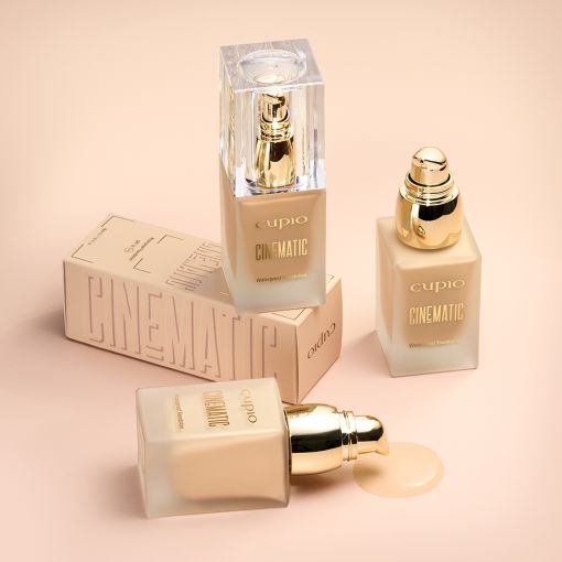 cinematic_all_1_1_1_1_1_1_1 Drei Flaschen Cinematic Makeup Foundation von Cupio mit goldenen Details auf einem sanften Hintergrund